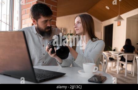 Selbstbewusste freiberufliche Fotografin Frau im Café mit männlichem Kunden, mit Laptop arbeiten und Bilder vor der Kamera ansehen. Neue moderne Technologien Stockfoto