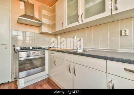 Beleuchtete Schränke mit Waschbecken und Geräten befinden sich in einer geräumigen, hellen Küche in einer modernen Wohnung Stockfoto