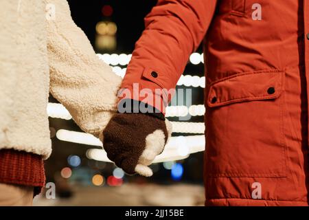 Horizontale Nahaufnahme eines unerkennbaren jungen Mannes und einer Frau, die am Winterabend gemeinsam im Freien die Hände halten Stockfoto