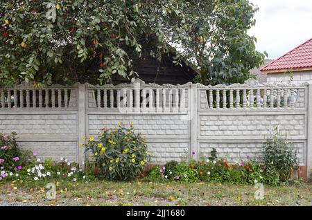 Eine alte klassische Balustrade im Freien mit Blumen. Antikähnlicher Steinzaun mit Säulen in der Nähe der europäischen Vorstadthütte Stockfoto