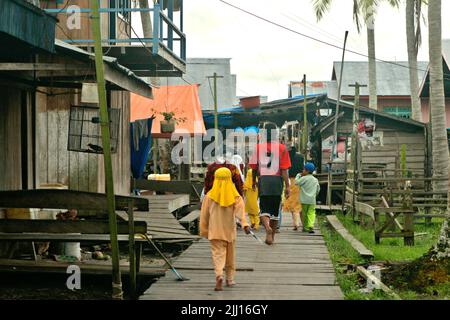 Dorfbewohner, die auf einem Holzsteg in Kasai, einem Küstendorf, in dem der Lebensunterhalt in erster Linie von Fischerei und Meeresressourcen abhängt, in Berau, Ost-Kalimantan, Indonesien, wandern. Stockfoto