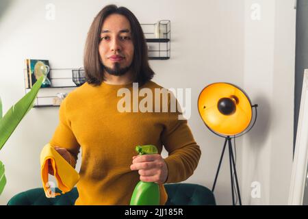 Ein schwarzhaariger Mann in einem Pullover mit einem Bart, der grüne Handsprüher hält, und einem Tuch in den Händen. Hochwertige Fotos Stockfoto