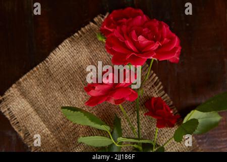 Rote Rosen Hintergrund auf Sacking auf Holzhintergrund. Geschenk, Geschenke. Speicherplatz kopieren. Stockfoto