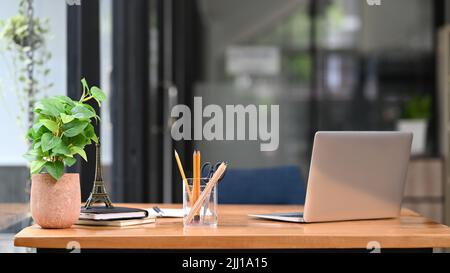 Büroschreibtisch aus Holz mit Laptop-Computer, Notizbüchern, Bleistifthalter und Topfpflanze Stockfoto