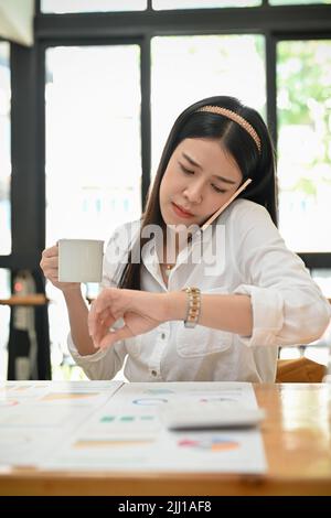 Porträt, seriöse und geschäftige, tausendjährige asiatische Geschäftsfrau oder Marketingmanagerin, die ihre Armbanduhr anschaut, um die Zeit zu überprüfen, während sie einen ph-wert hat Stockfoto