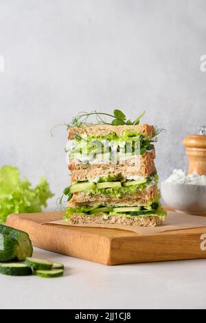 Englische Tee-Sandwiches mit Ricotta, Gurke, Microgreens und Dill auf grauem Hintergrund. Nahaufnahme. Vertikales Format. Stockfoto