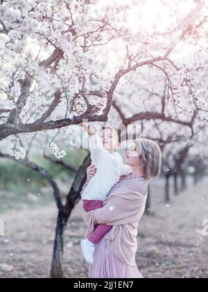 Mutter mit kleinem Sohn im Frühlingsgarten während der goldenen Stunde. Mutter und Sohn sind in der Natur aktiv. Familienspaziergänge in einem Frühlingsgarten. Alles gute zum Tag der Mutter Stockfoto