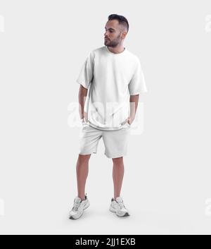 Übergroßes weißes T-Shirt-Modell, Shorts auf bärtigen Kerl in Sneakers, mit Händen in den Taschen, Vorderansicht, isoliert auf dem Hintergrund. Vorlage für Herren, Fash Stockfoto