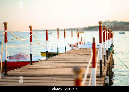Stimmungsvoller hölzerner Steg über dem wunderschönen Strand mit blauem Himmel, hölzerner Steg mit kleinen Booten bei Sonnenuntergang im Sommer. Stockfoto