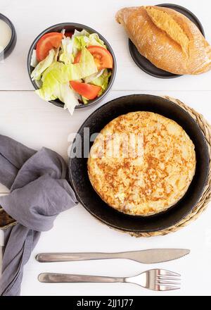 Tortilla, spanisches Omelett aus Eiern und Kartoffeln auf einem Holztisch. Traditionelle spanische Tapas oder Snacks mit Salat und Brot. Stockfoto