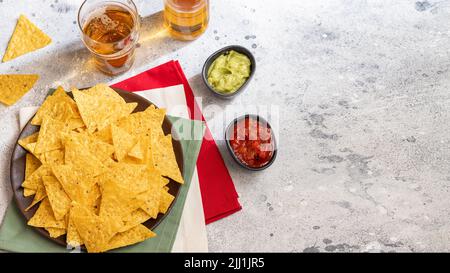 Berühmten Mexikanischen Imbiss, Nachos mit Guacamole, roter Chili Sauce und Bier auf Zement Hintergrund. Ansicht von oben. Stockfoto