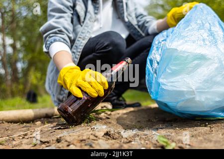 Eine Frau nimmt im Wald eine verlassene Glasflasche auf. Umweltmüllverschmutzung Stockfoto