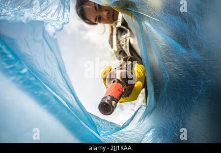 Nahaufnahme einer Frau, die Müll in eine Plastiktüte wirft. Blick von der Innenseite der Tasche. Das Konzept der Sorge um die Umwelt und des Recyclings Stockfoto