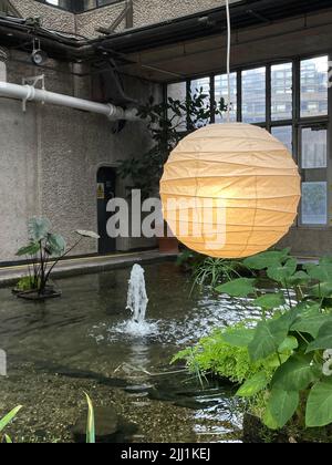Eine vertikale Aufnahme einer runden Laterne, die über einem Brunnen mit Pflanzen in einem botanischen Garten hängt Stockfoto