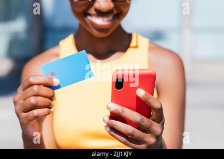 Smartphone und Kreditkarte auf den Händen einer nicht erkennbaren afrikanischen Frau. Konzept des Online-Shoppings Stockfoto