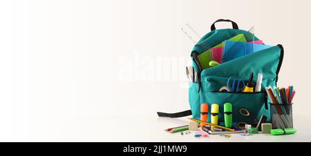 Blauer Schulrucksack voller Schulbedarf auf weißem Tisch und weißem isolierten Hintergrund. Vorderansicht. Panorama-Komposition. Stockfoto