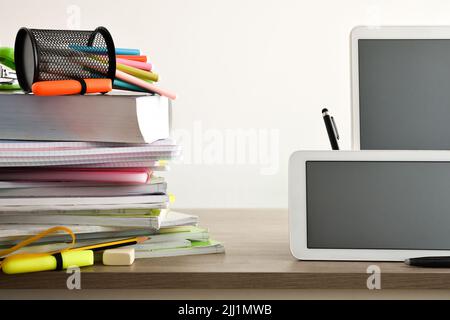 Pädagogischer Lernvergleich zwischen Schulbüchern und Notizbüchern mit elektronischen Gadgets auf Holztisch und isoliertem Hintergrund. Vorderansicht Stockfoto