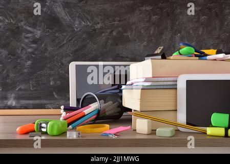 Schulbedarf und elektronische Geräte für den Unterricht auf Holztisch und Kreidetafel im Hintergrund. Vorderansicht Stockfoto