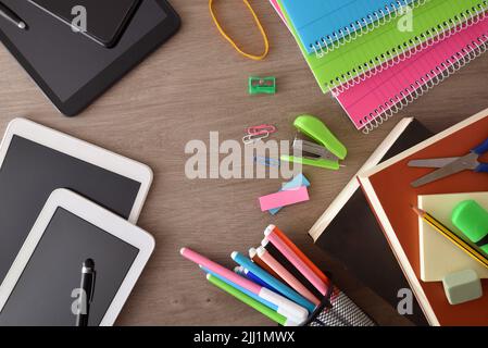 Pädagogischer Lernvergleich zwischen Schulbüchern und Notizbüchern mit elektronischen Gadgets auf Holztisch und isoliertem Hintergrund. Draufsicht. Stockfoto