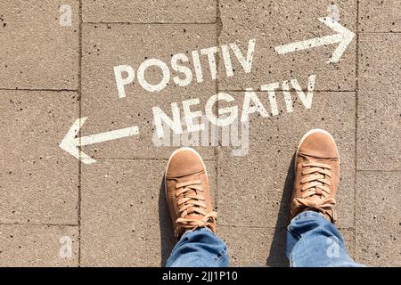 Ein brauner Schuh mit Text, der die Richtung zu positiv oder negativ auf einem Boden zeigt Stockfoto