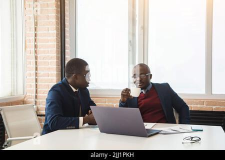Zwei afroamerikanische Geschäftspartner arbeiten gemeinsam an einem Laptop an einem gemeinsamen Projekt. Gegenseitige Unterstützung und Aufbau sozialer Kontakte Stockfoto
