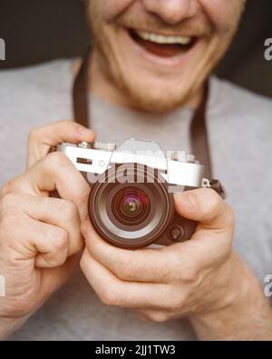 Ein glücklicher lächelnder Mann hält eine Kamera im Retro-Stil in der Hand und macht ein Foto. Nahaufnahme. Selektiver Fokus. Stockfoto