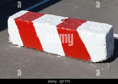 Betonblock mit Warnhinweis rot weiß diagonal gestreiften Muster liegt auf einer städtischen Straße Stockfoto