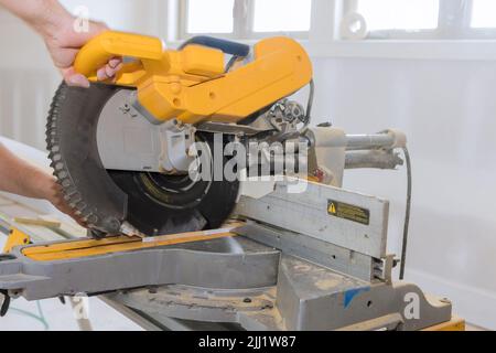 Um die Holzleisten und die Schonplatte fertigzustellen, schneidet ein Bauarbeiter mit einer Gehrungsäge Stockfoto