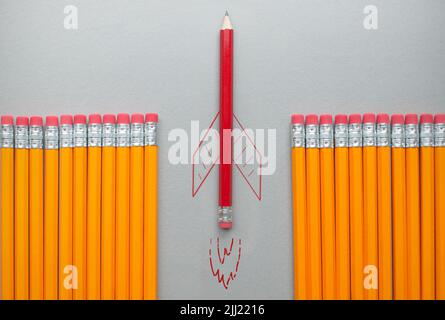 Roter Bleistift mit Raketenskizze, der sich zwischen einer Reihe orangefarbener Bleistifte heraussticht Stockfoto