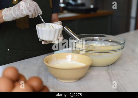 Hände in Gummihandschuhe rühren Teig für einen Kuchen Stockfoto