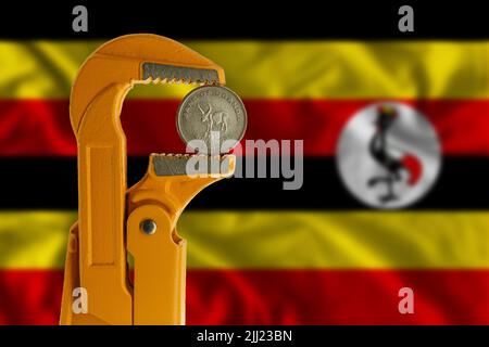 Einhundert Schillinge Uganda-Münze in einem orangefarbenen Klempnerschlüssel auf dem Hintergrund der Flagge Ugandas. Stockfoto