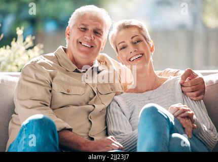 Unsere glücklichsten Erinnerungen wurden zu Hause gemacht. Porträt eines glücklichen Seniorenpaares, das sich zu Hause auf dem Sofa entspannt. Stockfoto