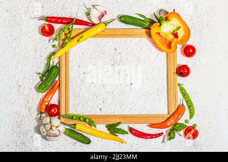 Verschiedene frische Gemüse und Gewürze rund um den Holzrahmen. Reife gelbe Paprika, Tomate, Erbse, Gurke, Knoblauch, Bunte Chilischoten. Zutaten zum Kochen Stockfoto