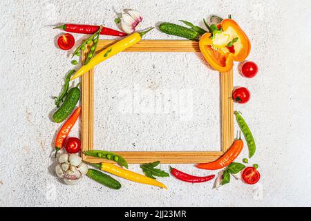 Verschiedene frische Gemüse und Gewürze rund um den Holzrahmen. Reife gelbe Paprika, Tomate, Erbse, Gurke, Knoblauch, Bunte Chilischoten. Zutaten zum Kochen Stockfoto