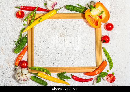 Verschiedene frische Gemüse und Gewürze rund um den Holzrahmen. Reife gelbe Paprika, Tomate, Erbse, Gurke, Knoblauch, Bunte Chilischoten. Zutaten zum Kochen Stockfoto