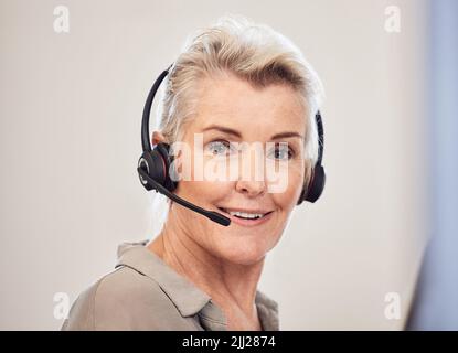 Wie kann ich Ihnen dabei zur Verfügung stehen? Porträt einer älteren Geschäftsfrau, die ein Headset trägt, während sie in einem Büro arbeitet. Stockfoto