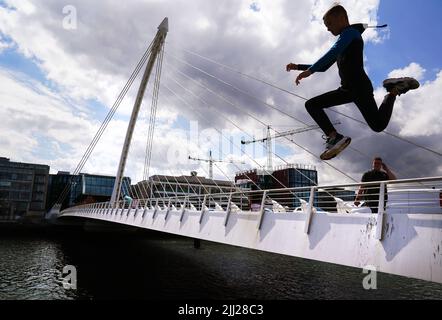 Ein Junge springt an einem Sommertag im Stadtzentrum von Dublin von der Samuel Beckett Bridge in den Fluss Liffey. Bilddatum: Freitag, 22. Juli 2022. Stockfoto