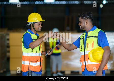 Glückliche asiatische Lagerarbeiter haben Spaß und Faustschlag während des Beginnens der Arbeit am Morgen. Stockfoto