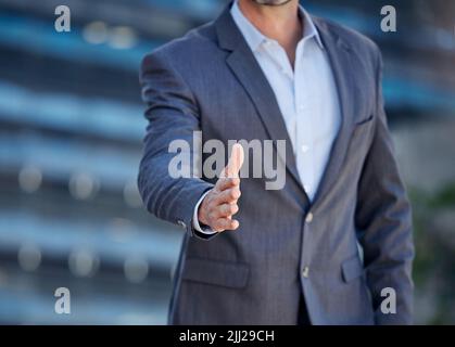 Ein nicht erkennbarer Geschäftsmann streckte seine Hand für einen Handschlag vor einem Stadthintergrund aus. Stockfoto