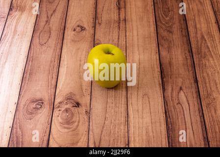 Ein einsamer goldener Apfel auf einem ungelackierten Holztisch Stockfoto