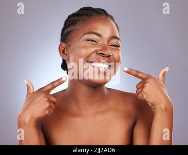 Es ist das Lächeln, oder? Studioaufnahme einer schönen jungen Frau, die auf ihr Lächeln zeigt. Stockfoto