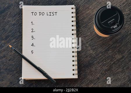 To Do Liste Wörter auf Notizblock mit Einweg-Kaffeetasse und Stift auf Holzschreibtisch geschrieben. Stockfoto