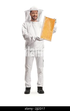 Junger männlicher Bienenzüchter in einer Uniform, der einen auf weißem Hintergrund isolierten Wabenrahmen hält Stockfoto