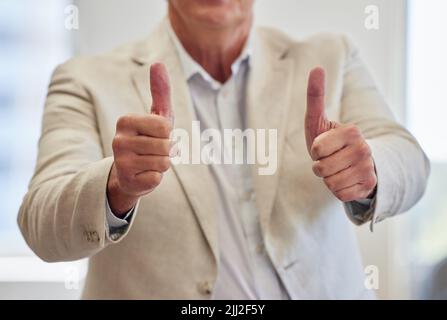 Wir haben es von hier aus abgedeckt. Ein nicht erkennbarer Geschäftsmann, der allein im Büro stand und einen Daumen nach oben zeigte. Stockfoto