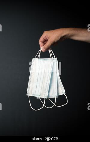 Männliche Hand hält eine einzelne covid medizinische Maske vor dunklem Hintergrund Stockfoto