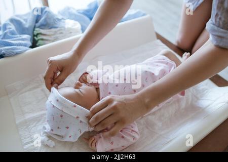 Mutter kleidet ihr neugeborenes Baby sorgfältig Stockfoto