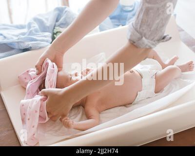 Mutter kleidet ihr neugeborenes Baby sorgfältig Stockfoto