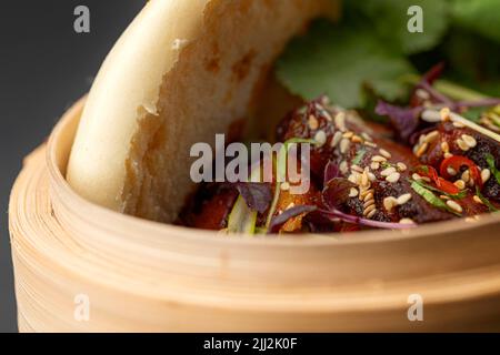 Scharfes Sandwich mit Schweinebauch, Gemüse und Koriander, serviert in einem haltbaren Behälter aus Naturmaterial Stockfoto