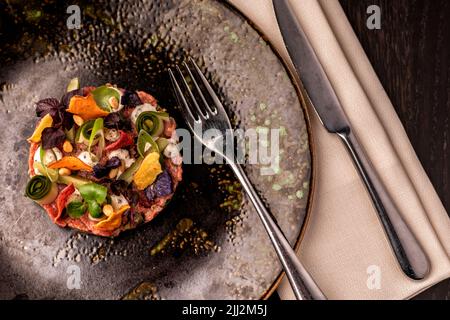 Eine wunderschöne, frisch zubereitete Thunfisch-Tartare mit süß-saurem Gemüse, Limettenmayonnaise, orientalischer Vinaigrette und Nori-Chips. Mit farbiger Platte, Stockfoto