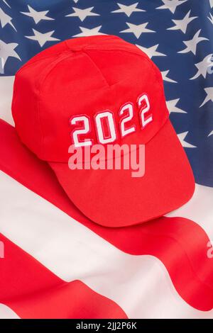 Rote MAGA-Kappe mit Datum 2022 und US Stars and Stripes-Flagge. Für die US-Zwischenwahlen vom 2022. November und die Ausrottung der Demokraten durch die US-Republikaner der Roten Welle. Stockfoto